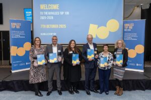 Award Winners standing on stage holding Kirklees Top-100 brochures.