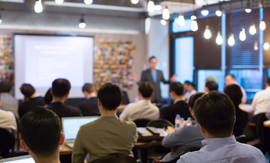 Delegates seated listening to a speaker presenting in from of a projected screen.