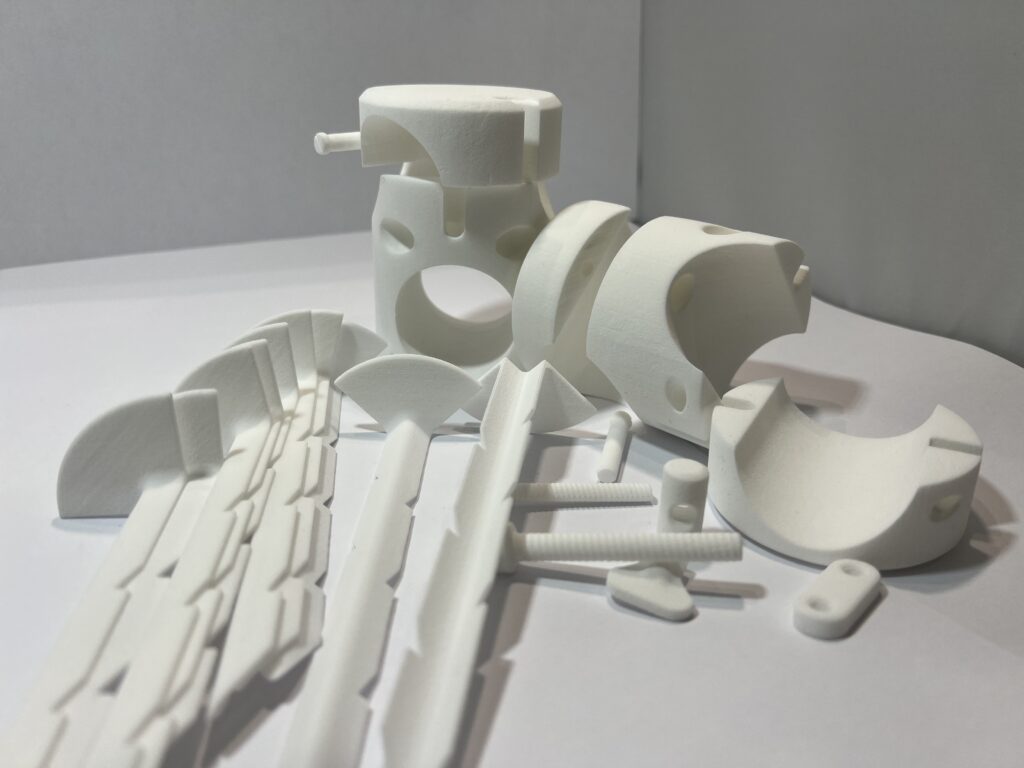 White 3D‑printed polymer components arranged on a surface, showing multiple parts produced for low‑volume additive manufacturing.