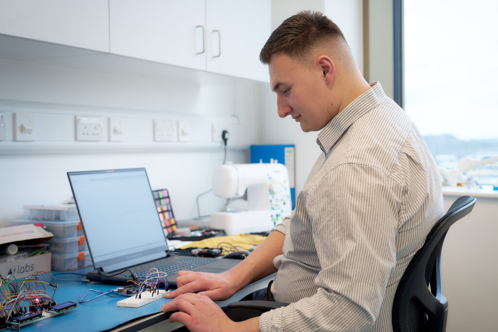 Person sat at a lab bench with a laptop open working on a proof of concept prototype for health innovators.