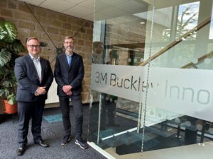 Two men stood next to each other smiling next to a glass sign saying 3M Buckley Innovation Centre.