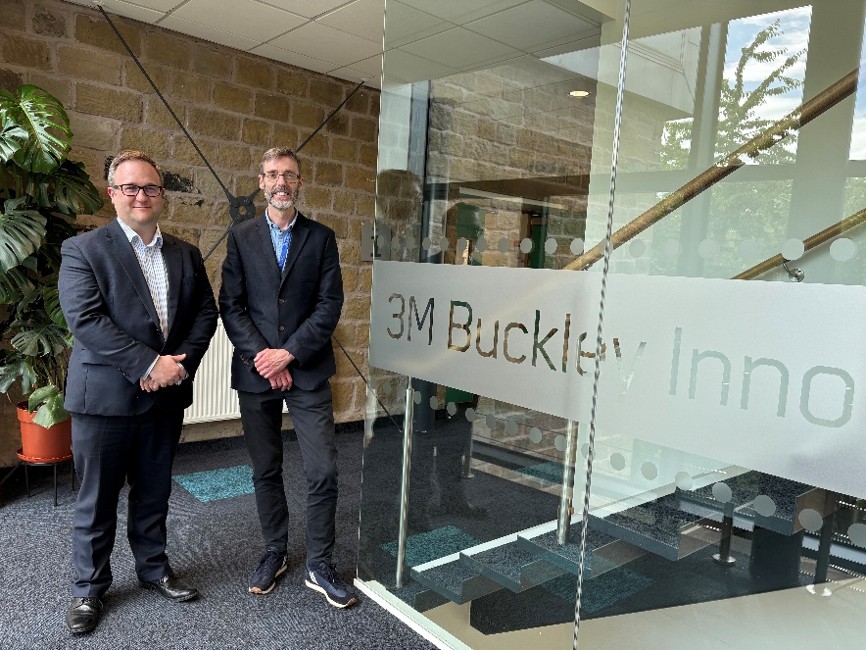 Two men stood next to each other smiling next to a glass sign saying 3M Buckley Innovation Centre.
